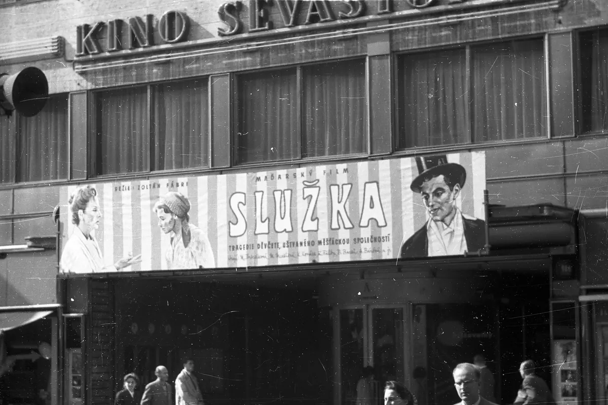 Черно-белая фотография фасада кинотеатра с надписью KINO SEVASTOPOL и большим киноафишем над входом, внизу мимо проходят люди